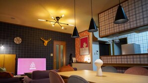 Ein modernes Wohnzimmer mit Essbereich, einem aufgehängten Hirschgeweih, einer großen Uhr und einem Fernseher, der das Airbnb-Logo zeigt.