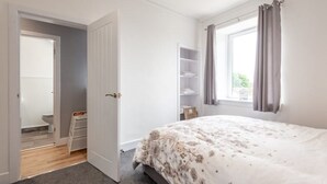 A bedroom with a bed, a wardrobe, a window with curtains, and a door leading to a bathroom. - No 65 Leuchars (Nr St Andrews) Free Parking - Pet Friendly (Leuchars)