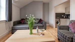 A modern living room with a grey sofa, a coffee table, and a kitchen area in the background. - No 65 Leuchars (Nr St Andrews) Free Parking - Pet Friendly (Leuchars)