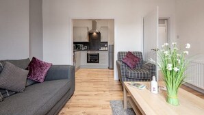 A modern living room with a grey sofa, a plaid sofa, a wooden coffee table, and a vase with white flowers. - No 65 Leuchars (Nr St Andrews) Free Parking - Pet Friendly (Leuchars)