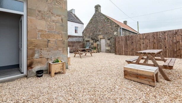 A stone building with a gravel patio, wooden benches, and a wooden fence. - No 65 Leuchars (Nr St Andrews) Free Parking - Pet Friendly (Leuchars)