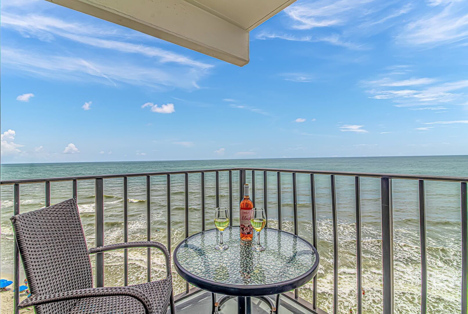 A balcony with a glass table and wicker chairs, overlooking the ocean.
