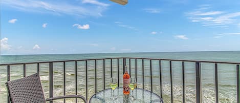 A balcony with a glass table and wicker chairs, overlooking the ocean.