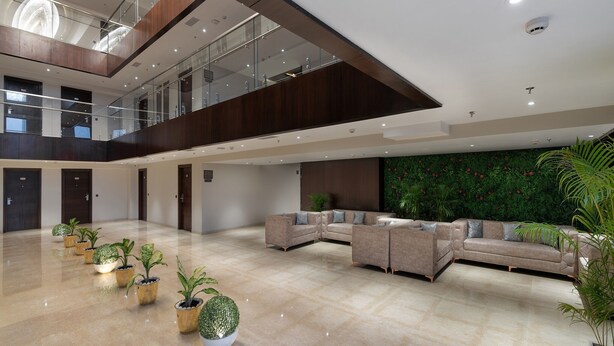 A spacious lobby with a high ceiling, a mezzanine level, a large seating area, and a green wall with plants. - Cygnett Park BL (Jaipur)