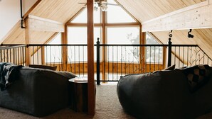 Une pièce mansardée chaleureuse, avec un plafond en pente, une rambarde en métal noir et deux fauteuils en forme de sac.