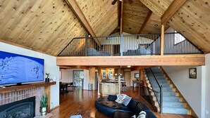 Un vaste espace de vie doté d’une cheminée, d’un grand téléviseur à écran plat, d’un canapé confortable et d’un escalier menant à l’étage supérieur.
