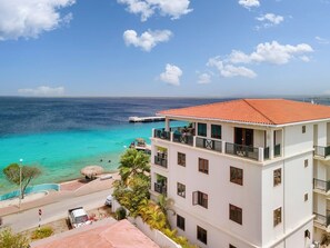 Ein mehrstöckiges Gebäude mit Balkonen, das auf ein türkisblaues Meer blickt.