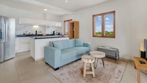 A modern kitchen with white cabinets and a central island, a light blue sofa, a small round table, and a bench. - Chachacha Apartment At Sea with spectacular views and dining with an ocean view (Kralendijk)