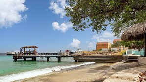 A beach with a pier, a thatched-roof structure, and a building with a red roof. - Chachacha Apartment At Sea with spectacular views and dining with an ocean view (Kralendijk)