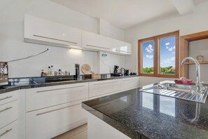 Una cocina moderna con armarios blancos, encimera de granito y ventana con vista a zonas verdes.