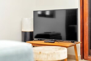 Una sala de estar moderna con un televisor de pantalla plana sobre un mueble de madera, un control remoto y una lámpara en una mesita.