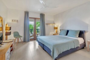 A hotel room with a bed, bedside tables, a desk with a chair, a lamp, and a view through a sliding door to an outdoor area. - Chachacha Apartment At Sea with spectacular views and dining with an ocean view (Kralendijk)