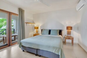 A bedroom with a bed, two bedside tables, a ceiling fan, and a view through a glass door. - Chachacha Apartment At Sea with spectacular views and dining with an ocean view (Kralendijk)