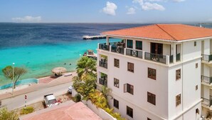 A multi-story hotel with balconies overlooking a turquoise sea, a clear sky, and a distant pier. - Chachacha Apartment At Sea with spectacular views and dining with an ocean view (Kralendijk)
