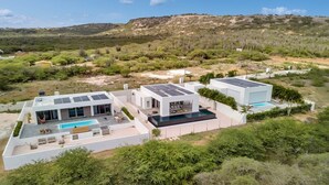 Uma casa moderna de dois andares com piscina, painéis solares e vista para a paisagem ao redor.