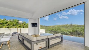 Uma sala de estar moderna com uma janela grande, um sofá, uma TV e um espaço de jantar.