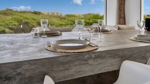 Mesa de jantar posta com pratos, talheres e copos, com vista para uma paisagem deslumbrante.