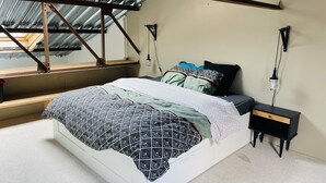 A bedroom with a skylight, a bed with patterned bedding, a bedside table, and a nightstand. - Loft Chaleureux à 200 Mètres de la Plage (Wimereux)