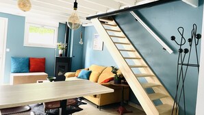 A modern living room with a wooden staircase, a dining table, and a sofa with cushions. - Loft Chaleureux à 200 Mètres de la Plage (Wimereux)