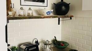 A kitchen with a white tiled backsplash, a black kettle, a white bowl with blue flowers, a clear glass bottle, a green bowl, a toaster, and a juicer. - Loft Chaleureux à 200 Mètres de la Plage (Wimereux)