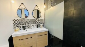 A bathroom with a white sink, two mirrors, patterned tiles, and a black tiled wall. - Loft Chaleureux à 200 Mètres de la Plage (Wimereux)