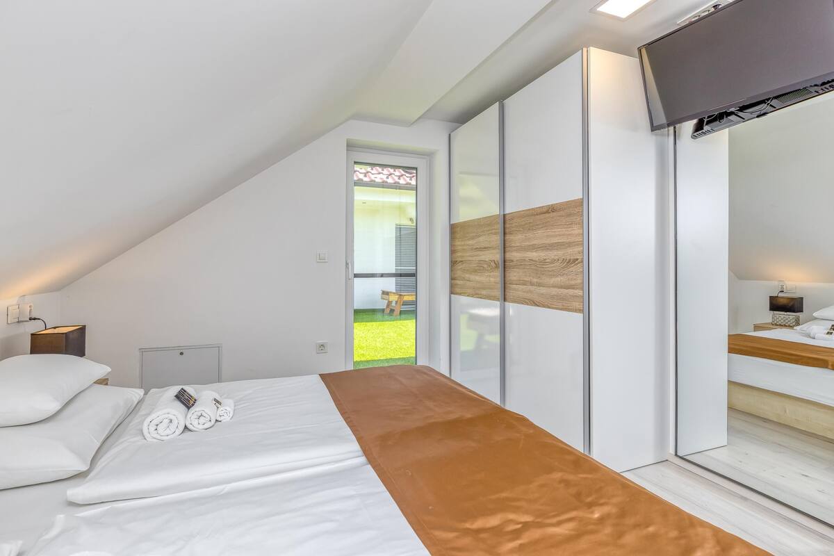 Un dormitorio moderno con una cama, un televisor y una puerta corredera que da a un balcón.