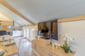 A modern kitchen with wooden cabinets, a large flat-screen TV, and a dining area with a table set for two. - Pool & Whirlpool Art Villas (Trebnje)