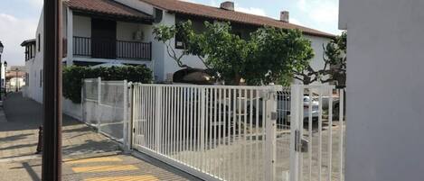 Un conjunto residencial cerrado con valla blanca, camino de entrada pavimentado y un edificio con tejado de tejas.