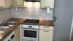 Una cocina compacta con armarios blancos, horno integrado, microondas y pileta.