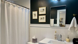 A bathroom with a white bathtub, a toilet, a sink with a mirror, and framed pictures on the wall. - Cozy Central Studio - Gunnison (Gunnison)