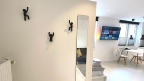 A modern room with a white wall, a large mirror, and three black wall-mounted figures. There is a TV mounted on the wall, a sofa, and a dining area with chairs and a table. - Apartment Schloofschdubb in Fuldatal Nähe Kassel (Fuldatal)