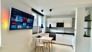 A modern kitchen with white cabinetry, a black countertop, and a dining area with white chairs. - Apartment Schloofschdubb in Fuldatal Nähe Kassel (Fuldatal)
