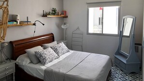 Une chambre à coucher comprenant un lit, une table de chevet, une lampe, un ventilateur de plafond, une fenêtre et un miroir.
