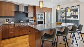 A modern kitchen with wooden cabinets, stainless steel appliances, a central island with bar stools, and pendant lighting. - The Lion at Vail W302 (Vail)