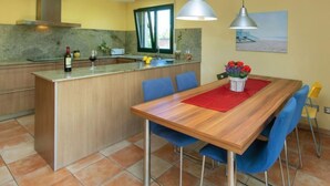 A modern kitchen with a central island, blue chairs, and a dining table with a red placemat. - Ullastreta by Interhome (La Bisbal D'Emporda)
