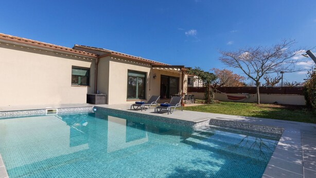 A swimming pool with tiled edges, a covered patio area with lounge chairs, and a house with a tiled roof and large windows. - Ullastreta by Interhome (La Bisbal D'Emporda)