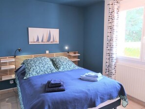 Une chambre à coucher avec un lit, une table de chevet, une lampe, une fenêtre avec des rideaux et un tableau au mur.