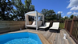 Un pontile in legno con piscina, poltrone da relax bianche e una struttura a tenda.