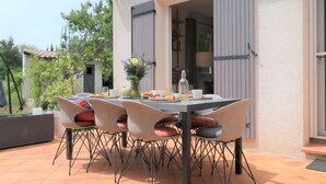Un'area pranzo all'aperto con un tavolo e sedie, un vaso con fiori e una bottiglia sul tavolo.