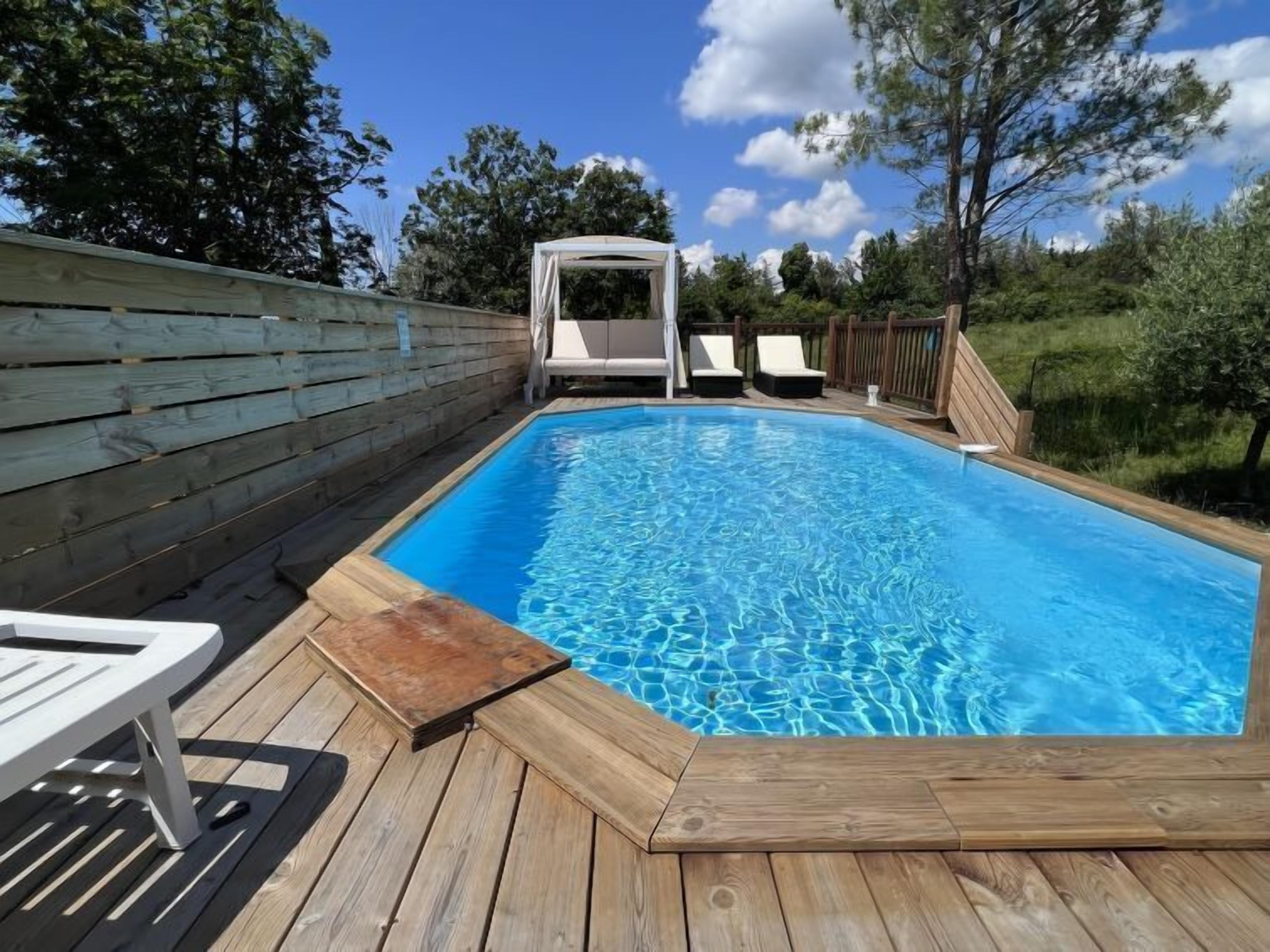 Una piscina rectangular con muelle de madera, rodeada por una valla de madera y árboles.