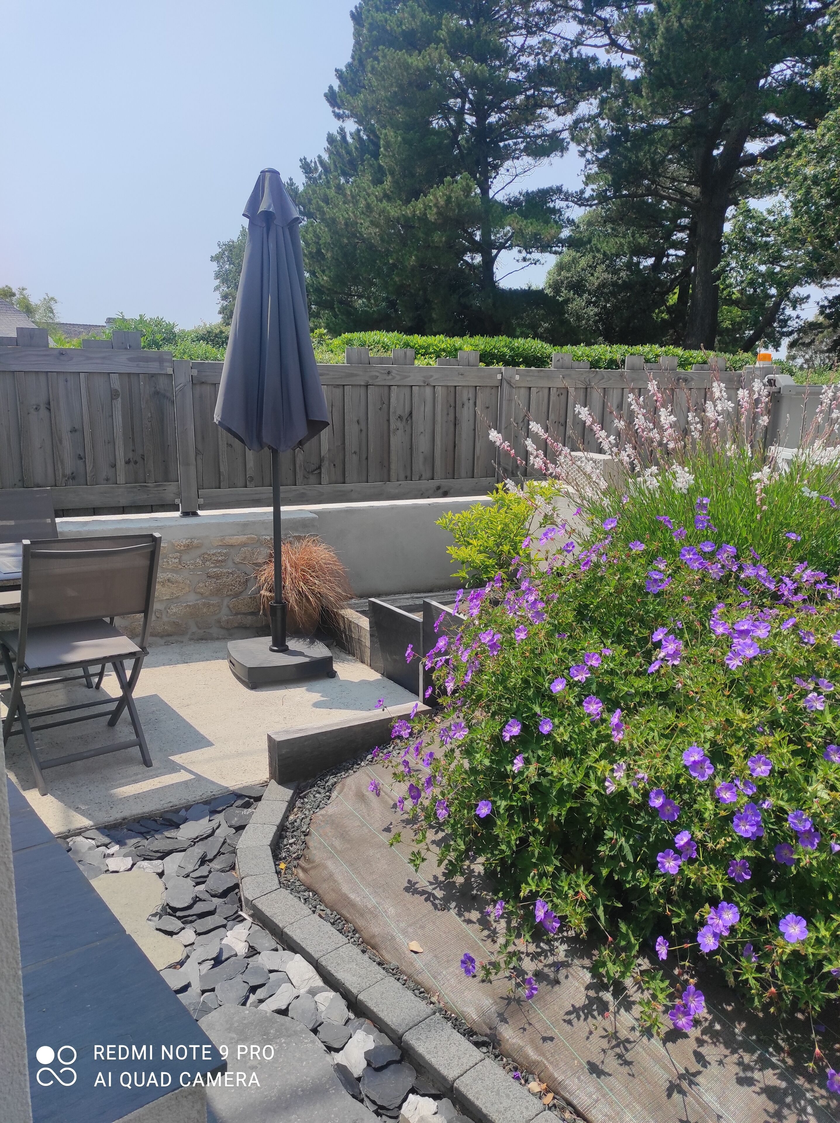 Eine Terrasse im Freien mit Holzlattenzaun, Tisch und Stühlen sowie ein Garten mit violetten Blumen.