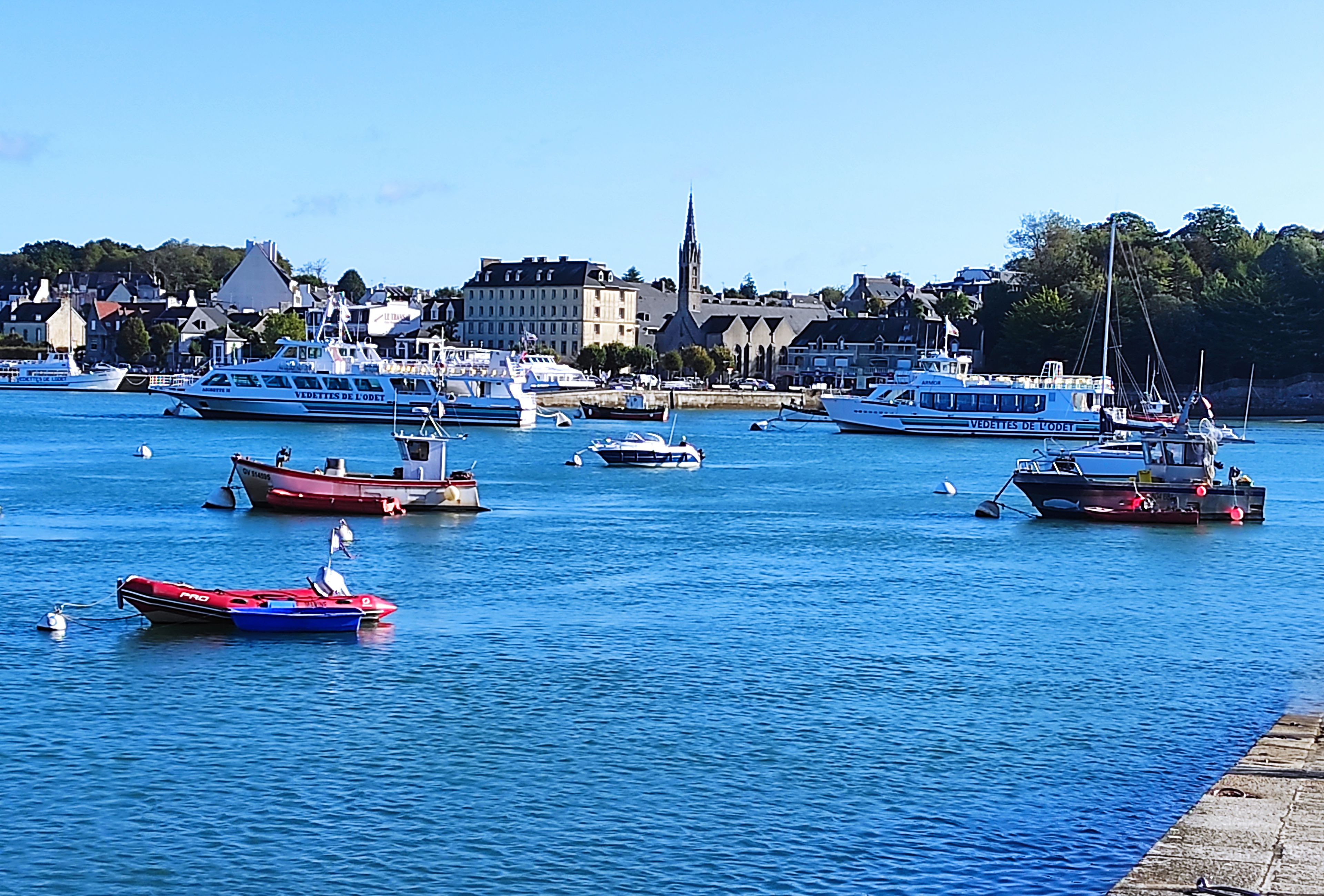 A harbor with various boats, including a large blue ferry and smaller fishing boats.