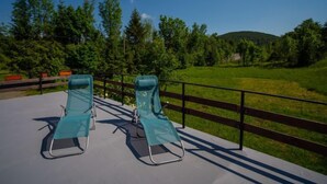 Duas cadeiras de descanso em um deck de concreto com cerca de madeira e vista para um campo verde e árvores.