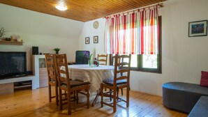 Uma sala de estar acolhedora com piso de madeira, uma mesa de jantar com cadeiras, uma televisão e um sofá.