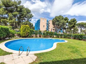 A swimming pool with a curved edge, surrounded by well-maintained grass and trees. - Bosc de la Montserrada by Interhome (La Pineda)