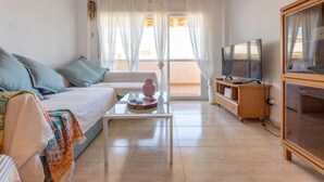 A modern living room with a sofa, a coffee table, a TV, and a balcony with curtains. - Bosc de la Montserrada by Interhome (La Pineda)