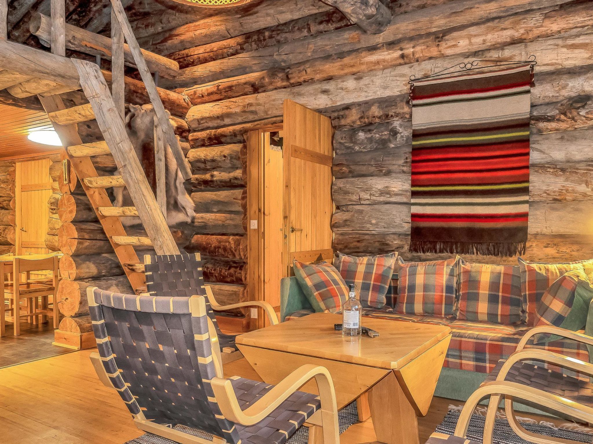 A log cabin interior with a wooden table, two chairs, a sofa, and a blanket.