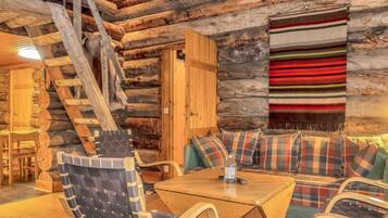 A log cabin interior with a wooden table, two chairs, a sofa, and a blanket.