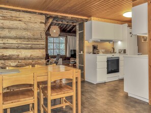 A log cabin interior with a wooden dining table and chairs, a kitchen with white cabinetry, and a stone fireplace. - Poromooli a1 by Interhome (Inari)