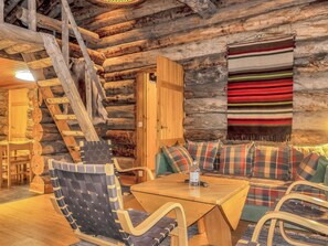 A log cabin interior with a wooden dining table, chairs, a sofa with plaid cushions, and a hanging tapestry. - Poromooli a1 by Interhome (Inari)